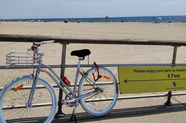 A bike leans next to a railing with the beach in the background in NYC.